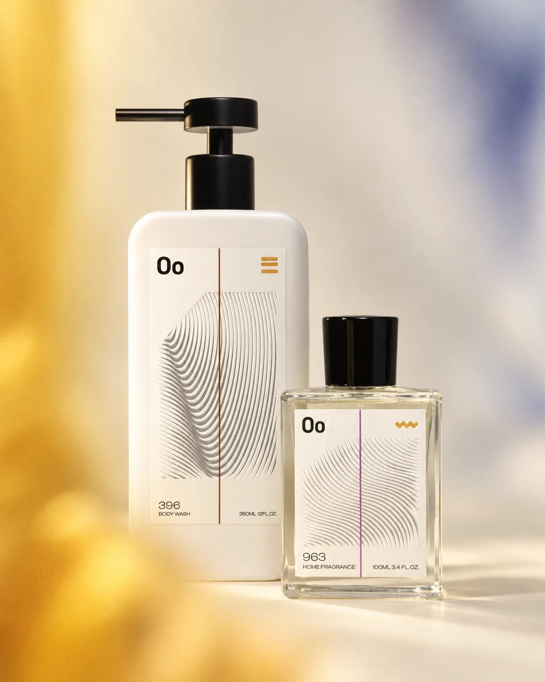 Oo La Lab body wash and clear home fragrance bottle together in warm ivory light
